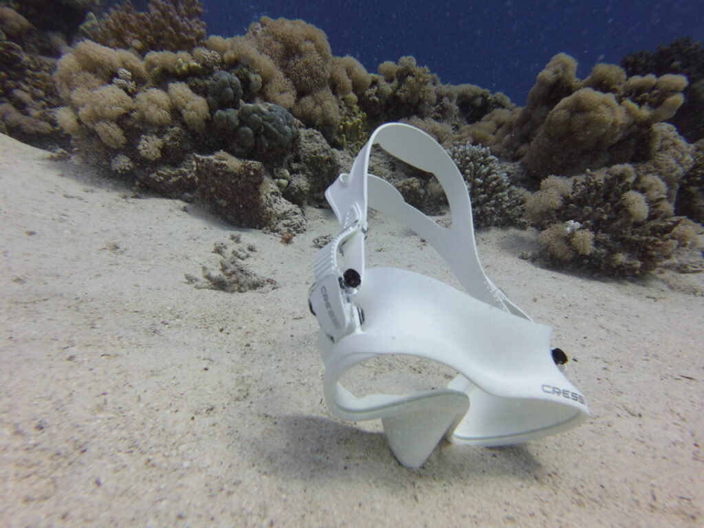 Cressi F1 scuba mask resting on seabed against coral reef background.