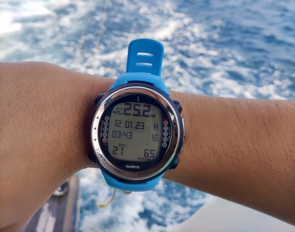 Suunto D4i dive computer on wrist against blue ocean background.