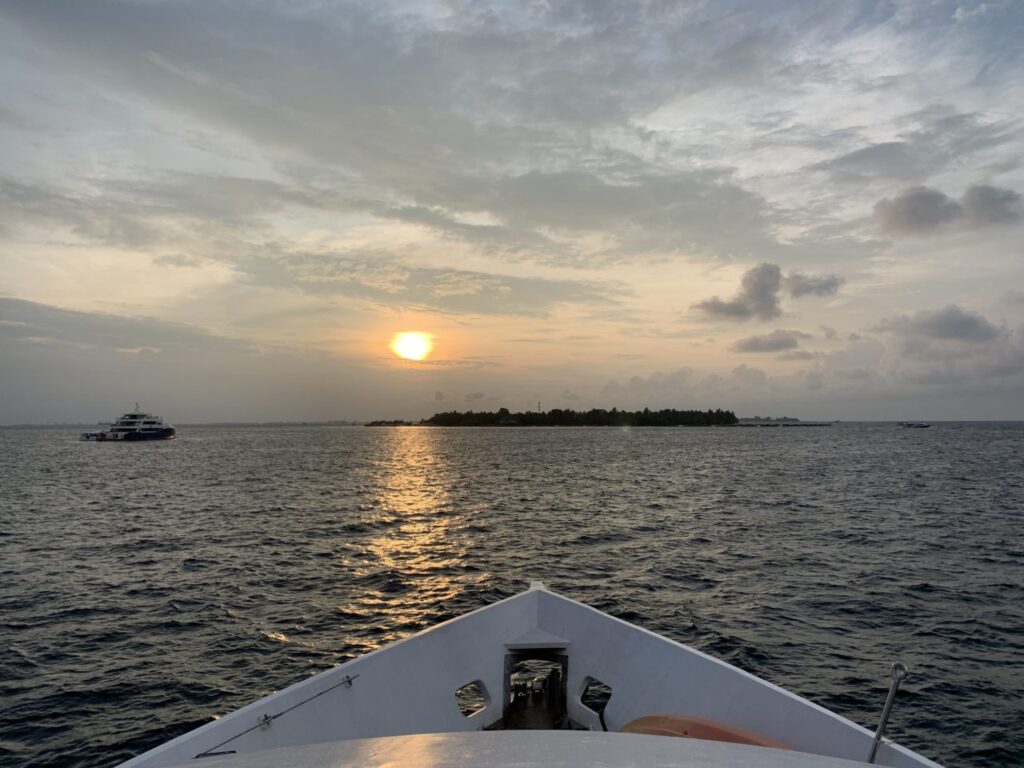 Bow of Maldives Liveaboard as it heads towards island with sunset behind it.