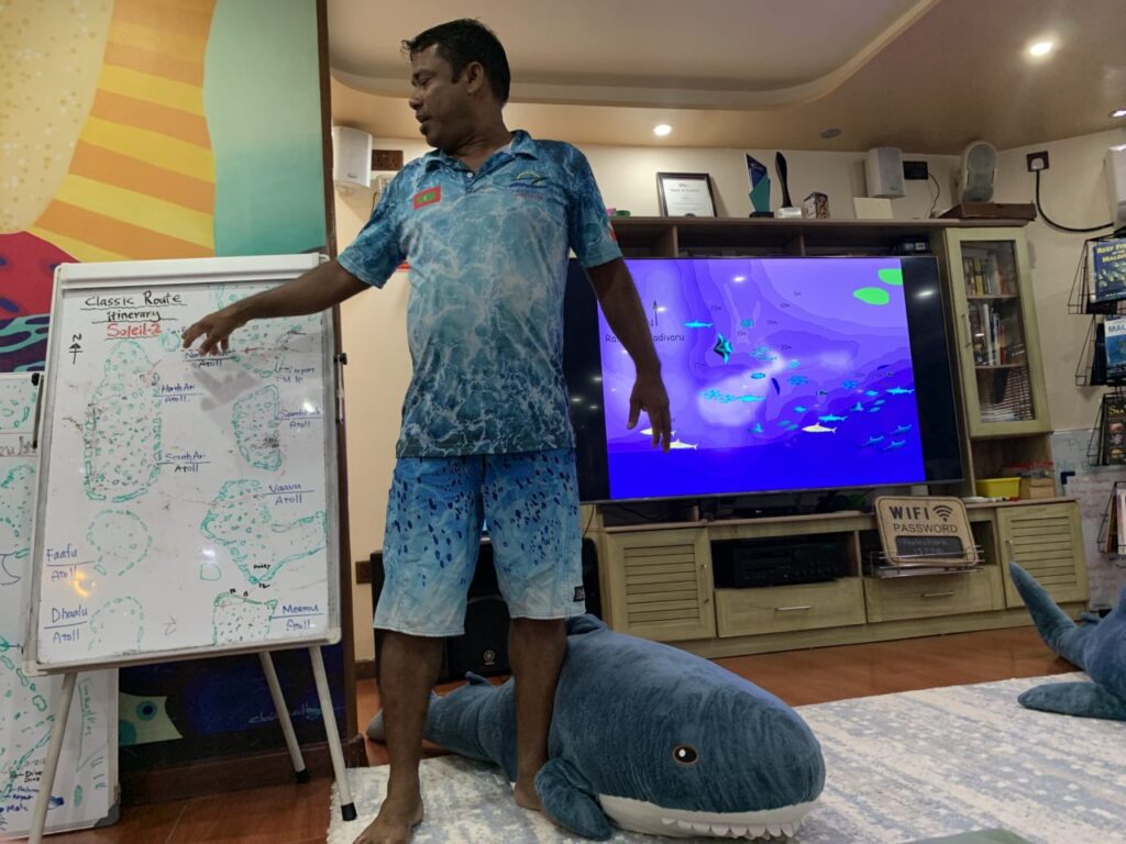 Liveaboard owner giving a dive briefing with whiteboard and projector screen.