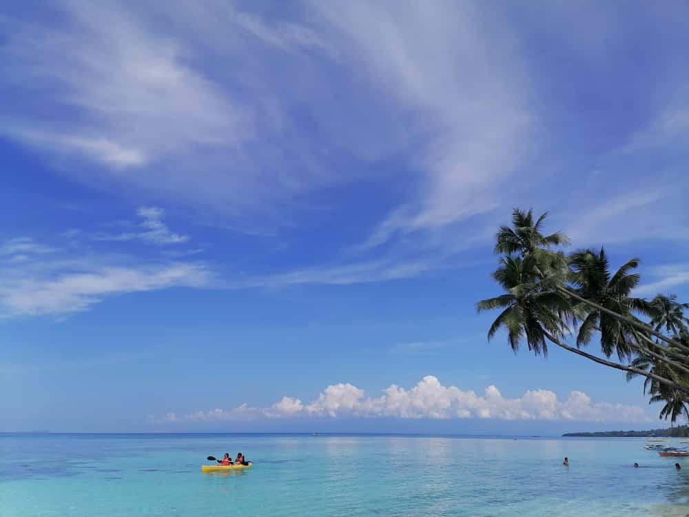 Calm blue ocean alongside beach of Siquijor island with kayakers in the distance.