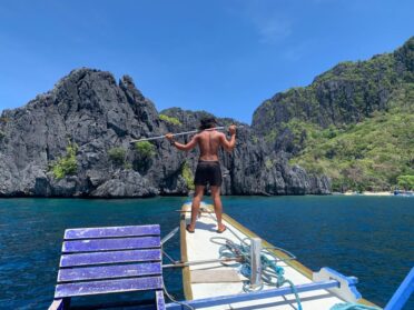 Dive boat with diving instructor surveying the dive sites of El Nido from above the water.