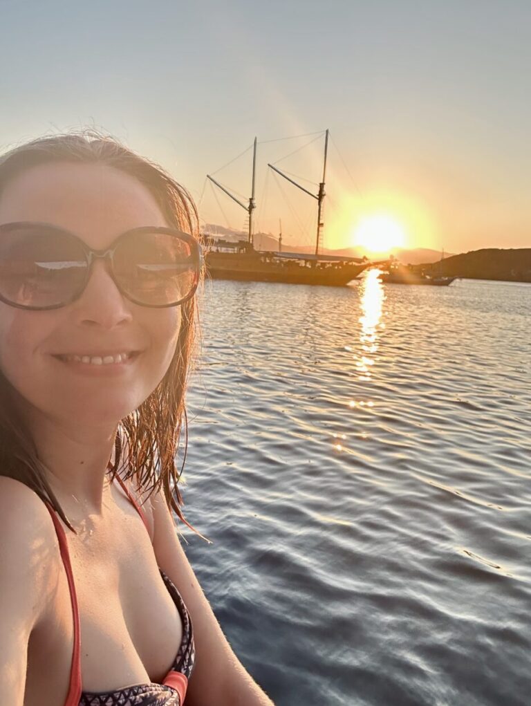 Selfie of Jasmin Rahimy on deck of the Akomo Isseki with a beautiful Sunset over the ocean and indonesian Phinisi boats in the background.