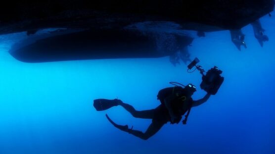 diver with camera underneath boat
