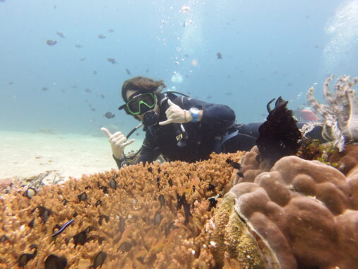 Cool scuba diver giving double rock on sign behind staghorn coral in Anilao, Batangas.