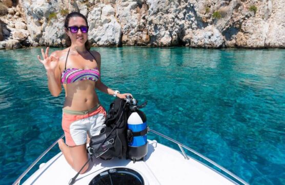 Woman diver on boat with bcd gives the ok sign.