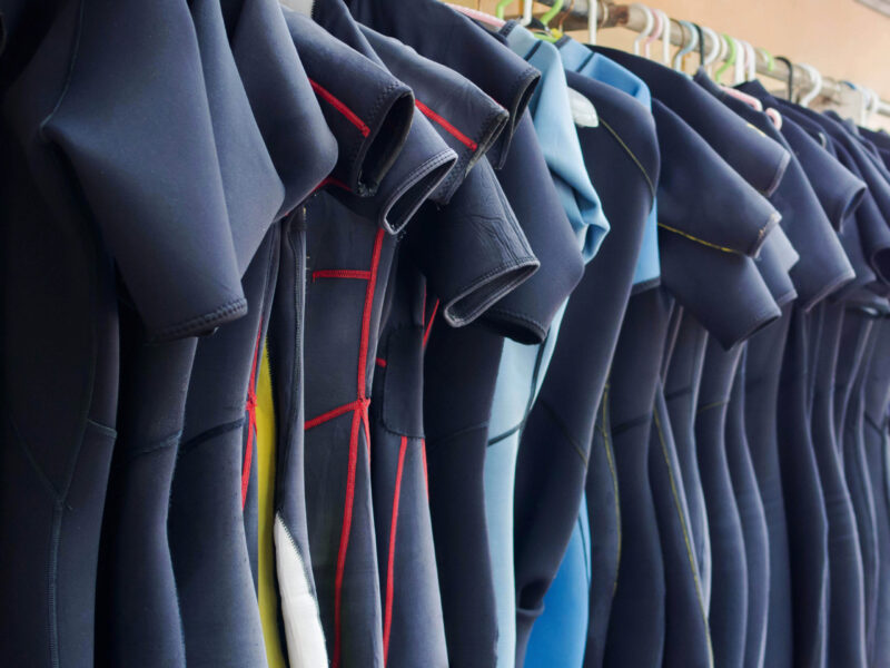 Line,Of,Multiple,Hanging,Wetsuits,At,Scuba,Diving,Center.